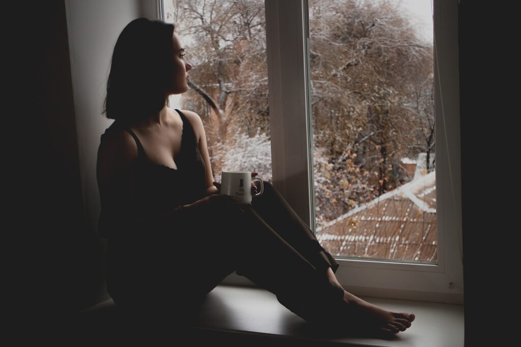 A woman sitting on a window while reflecting on procrastination. 